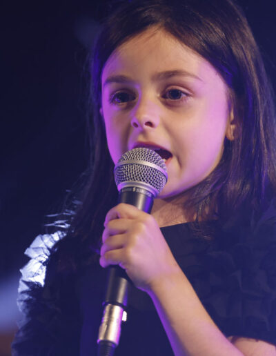 Bambina che canta con il microfono durante una performance di ArteMusica Piacenza