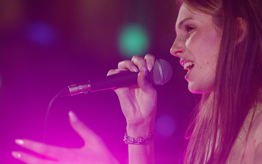 Cantante di ArteMusica Piacenza in primo piano mentre canta al microfono illuminata da luci rosa