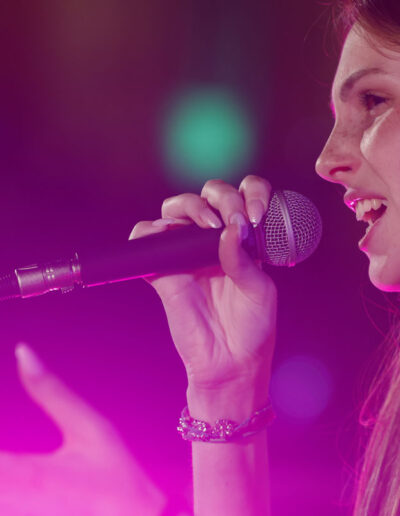Cantante di ArteMusica Piacenza in primo piano mentre canta al microfono illuminata da luci rosa
