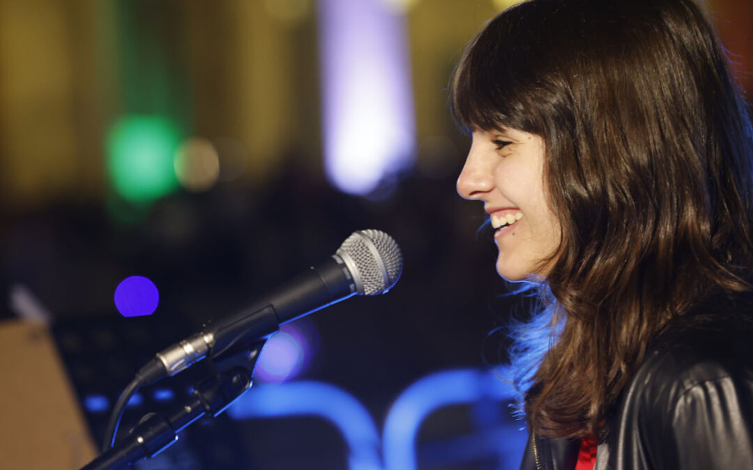 Giovane cantante di ArteMusica Piacenza che sorride mentre si esibisce al microfono durante un concerto serale