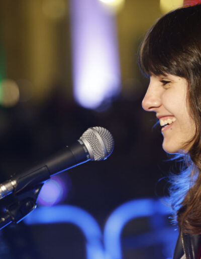 Giovane cantante di ArteMusica Piacenza che sorride mentre si esibisce al microfono durante un concerto serale