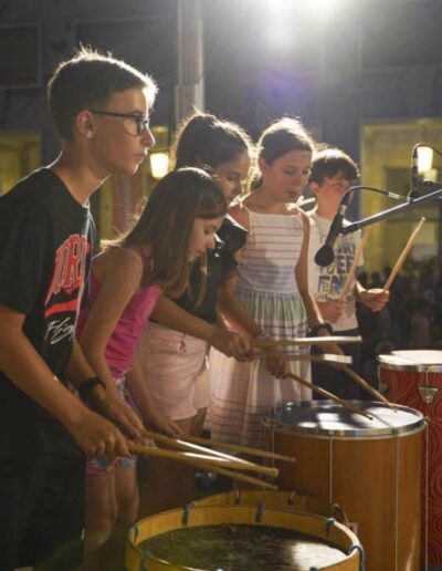 Gruppo di bambini che suonano percussioni sul palco durante un concerto a Piacenza