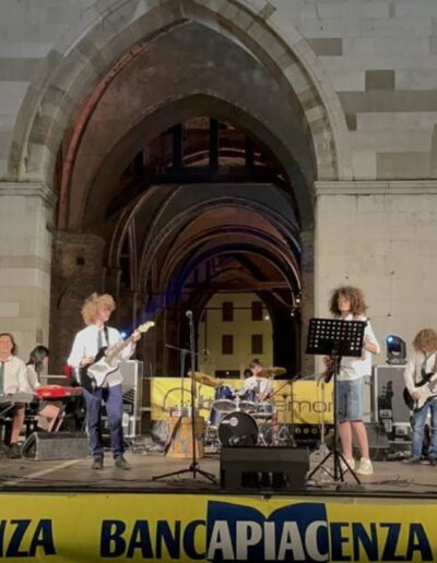 Band di giovani musicisti che si esibisce dal vivo sotto i portici di Piacenza durante un evento serale