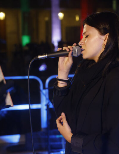 Cantante di ArteMusica Piacenza si esibisce dal vivo al microfono durante un concerto serale