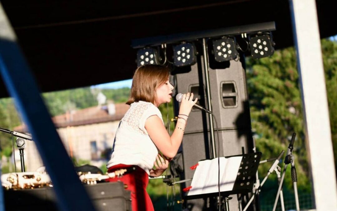 Giovane cantante si esibisce dal vivo su un palco all’aperto con microfono e leggìo