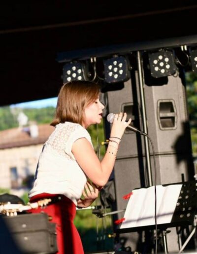 Giovane cantante si esibisce dal vivo su un palco all’aperto con microfono e leggìo