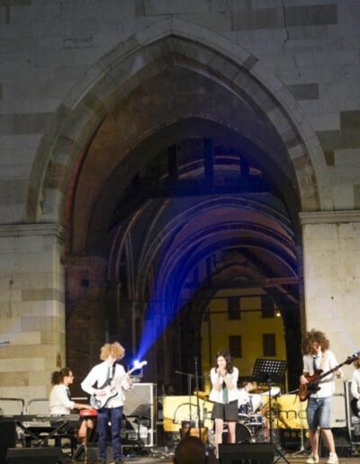 Band di giovani musicisti si esibisce sotto le arcate del Palazzo Gotico durante un concerto serale