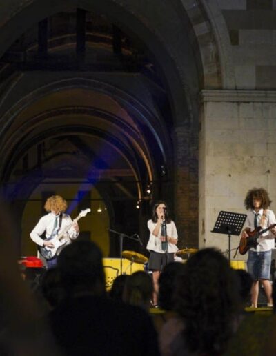 Band giovanile si esibisce di sera sotto le arcate del Palazzo Gotico davanti al pubblico