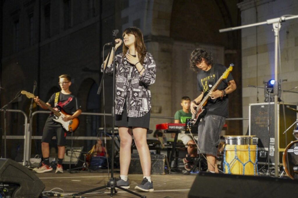 Concerto di giovani musicisti sul palco durante un evento serale in piazza.