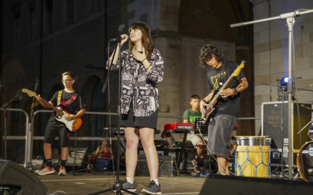 Concerto di giovani musicisti sul palco durante un evento serale in piazza.