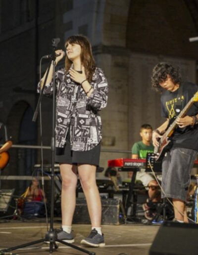 Concerto di giovani musicisti sul palco durante un evento serale in piazza.