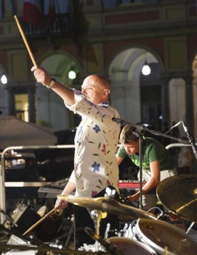 Insegnante di batteria sul palco con giovani musicisti durante un concerto a Piacenza