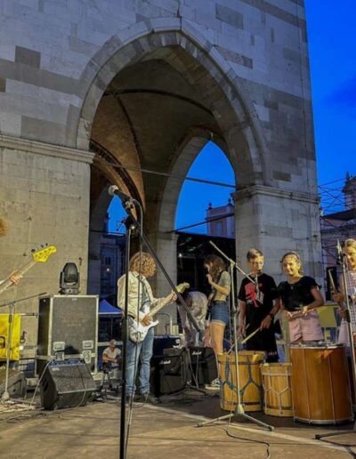Concerto serale in Piazza Cavalli a Piacenza con giovani musicisti e percussionisti sul palco durante un evento di musica scolastica.