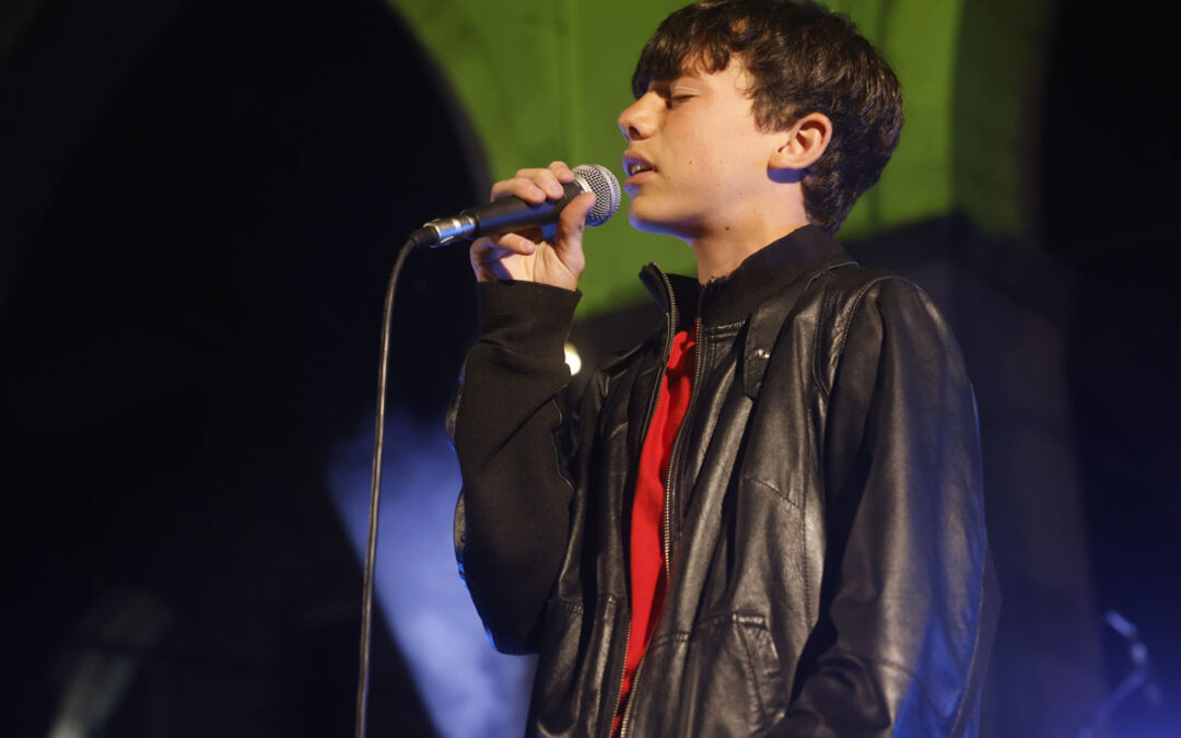 Giovane cantante di ArteMusica Piacenza che si esibisce dal vivo sul palco con microfono in mano