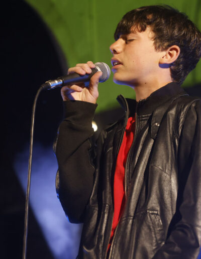 Giovane cantante di ArteMusica Piacenza che si esibisce dal vivo sul palco con microfono in mano