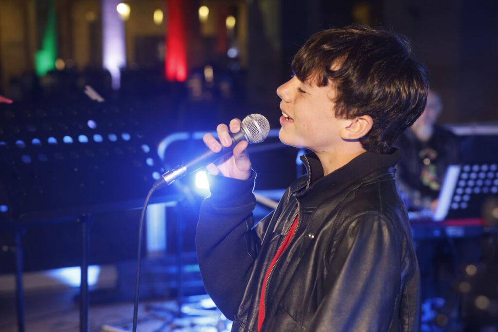 Giovane cantante di ArteMusica Piacenza che canta dal vivo sul palco tenendo il microfono