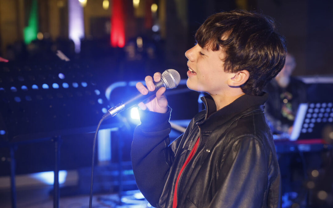 Giovane cantante di ArteMusica Piacenza che canta dal vivo sul palco tenendo il microfono