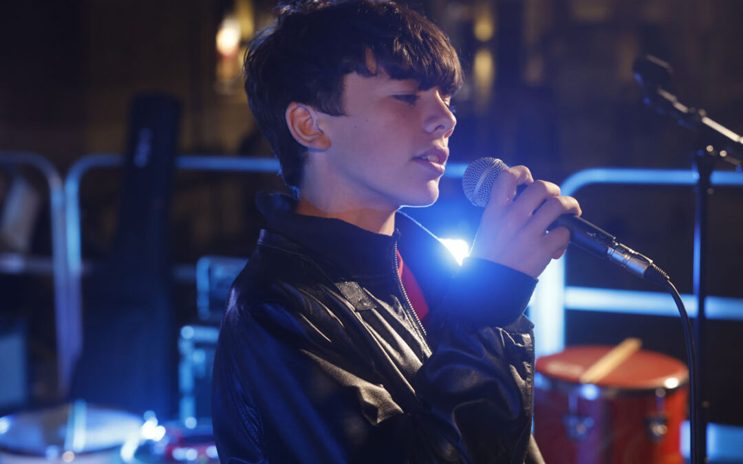 Giovane cantante di ArteMusica Piacenza che canta dal vivo tenendo il microfono sul palco