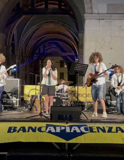 Giovane band che si esibisce dal vivo sotto i portici di Piacenza durante un evento serale