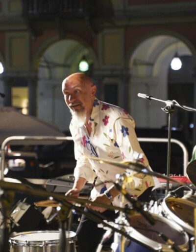 Insegnante che suona le percussioni sul palco insieme a giovani musicisti durante un concerto a Piacenza